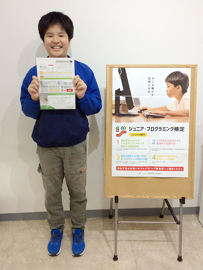 合格証明書を手にしてポスターの前でたっている受講生